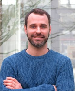 A person stands with arms crossed and looks friendly into the camera.