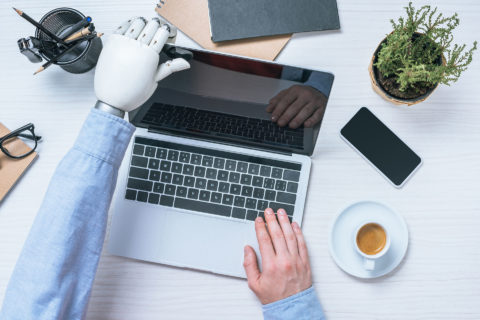 partial view of businessman with prosthetic arm opening laptop at table in office