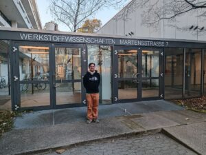 A man is standing in front of a building with glass doors.