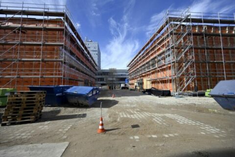 The photo shows two unfinished buildings framed with scaffolding, above blue sky with white clouds.