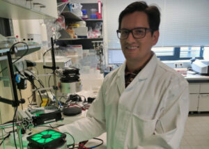 A man with glasses and a white coat stands in a laboratory.