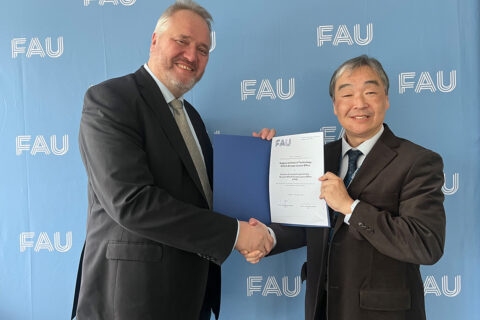 Two people in suits look kindly into the camera, they hold a certificate in their hands and shake hands.