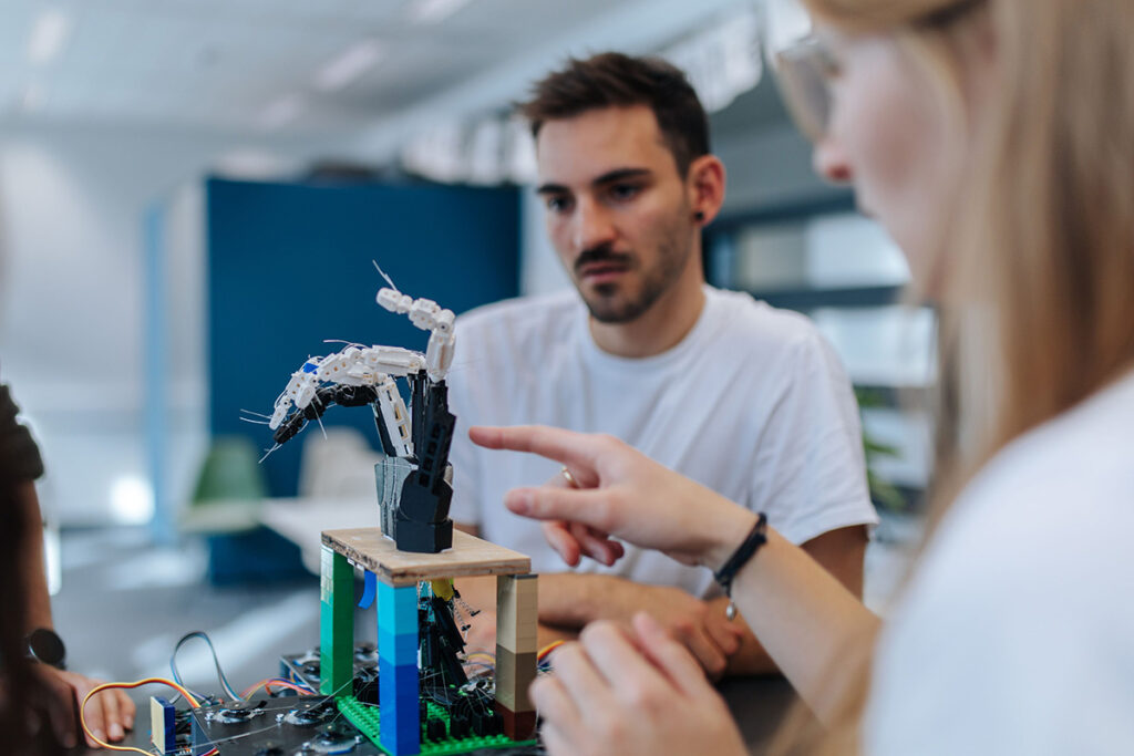 Two people are looking at a replica hand on a small table. The replica hand is connected with cables and is supposed to be able to move using electronic impulses.