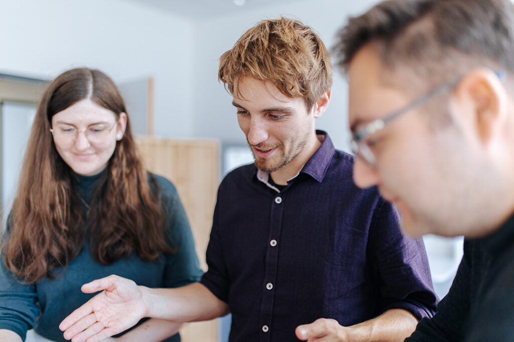 Three people stand next to each other and look down with a friendly smile.