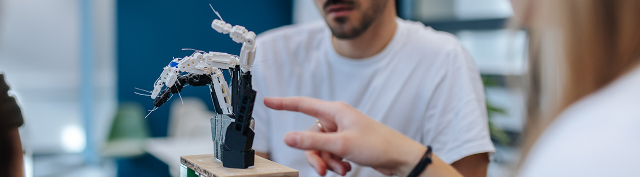 Two people are looking at a replica hand on a small table. The replica hand is connected with cables and is supposed to be able to move using electronic impulses.