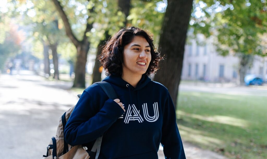 A young woman is wearing a blue hoodie and a bagpack while walking through a park.