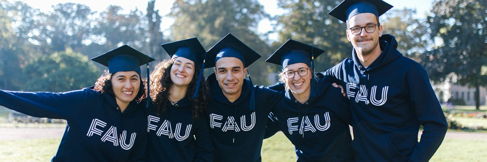 A group of five people are wearing blue hoodies and graduations hats while standing in a park.