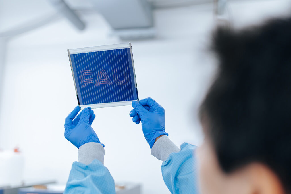 A person with blue gloves holds up a dark blue sign. FAU is printed on the sign.