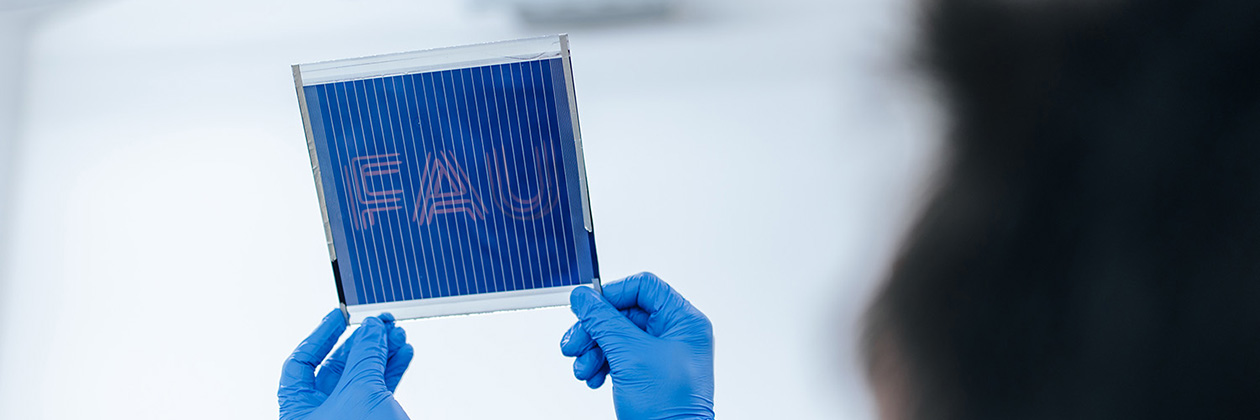 A person with blue gloves holds up a dark blue sign. FAU is printed on the sign.