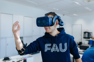 One person wears blue virtual reality glasses and looks at their own hand.