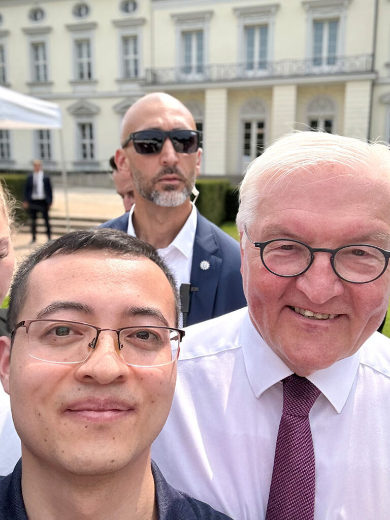 Three people are very much in front of the camera. The two people in front are smiling.