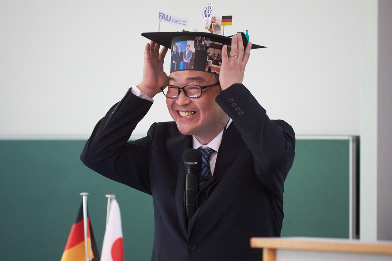 A person in a dark suit is holding a doctor's dog with both hands on his head. The person is wearing glasses and laughing.