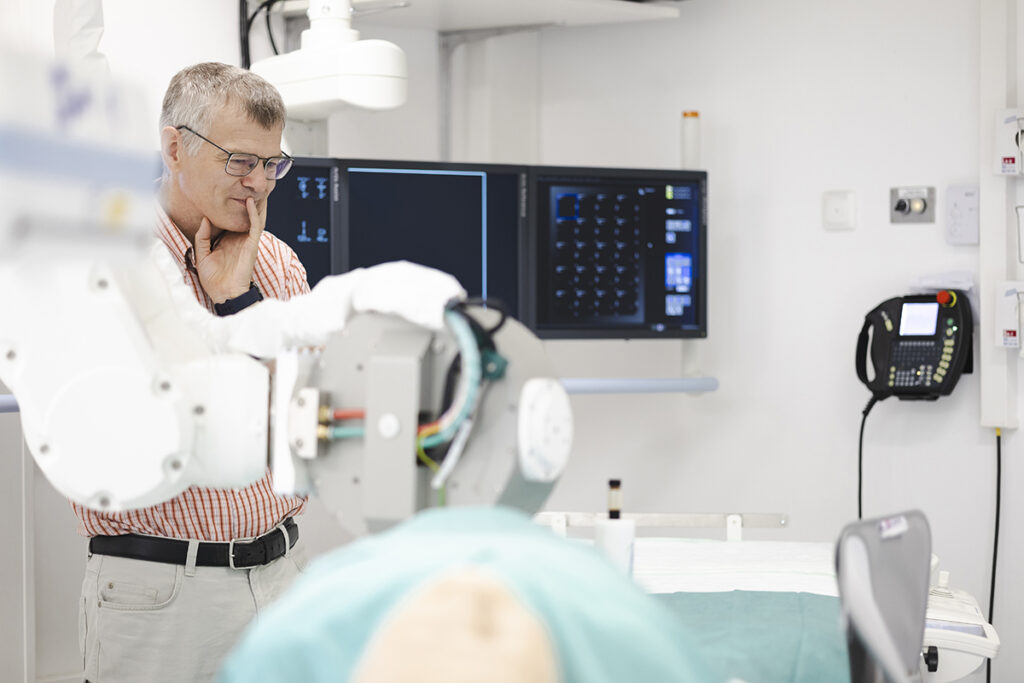 A person looks at a hospital bed with a robotic arm and screens in the background. (Bild: FAU/Boris Mijat)