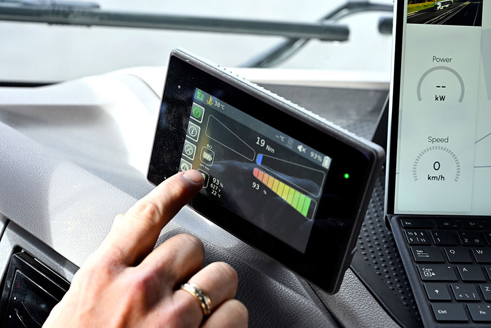 An index finger touches a small screen on a navigation device in a car.