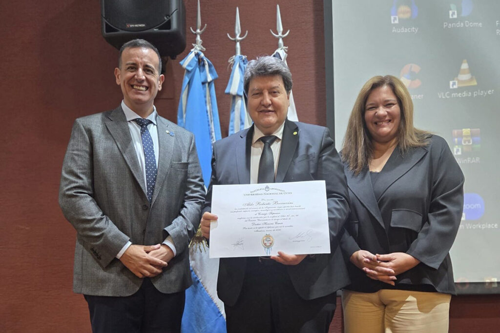 Three people are standing side by side, smiling at the camera. The person in the middle is holding a certificate in front of them.