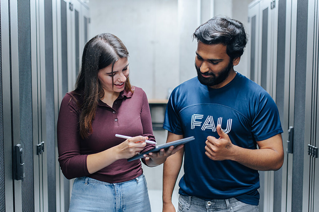 Two people are standing next to each other in a narrow corridor, looking at a tablet.