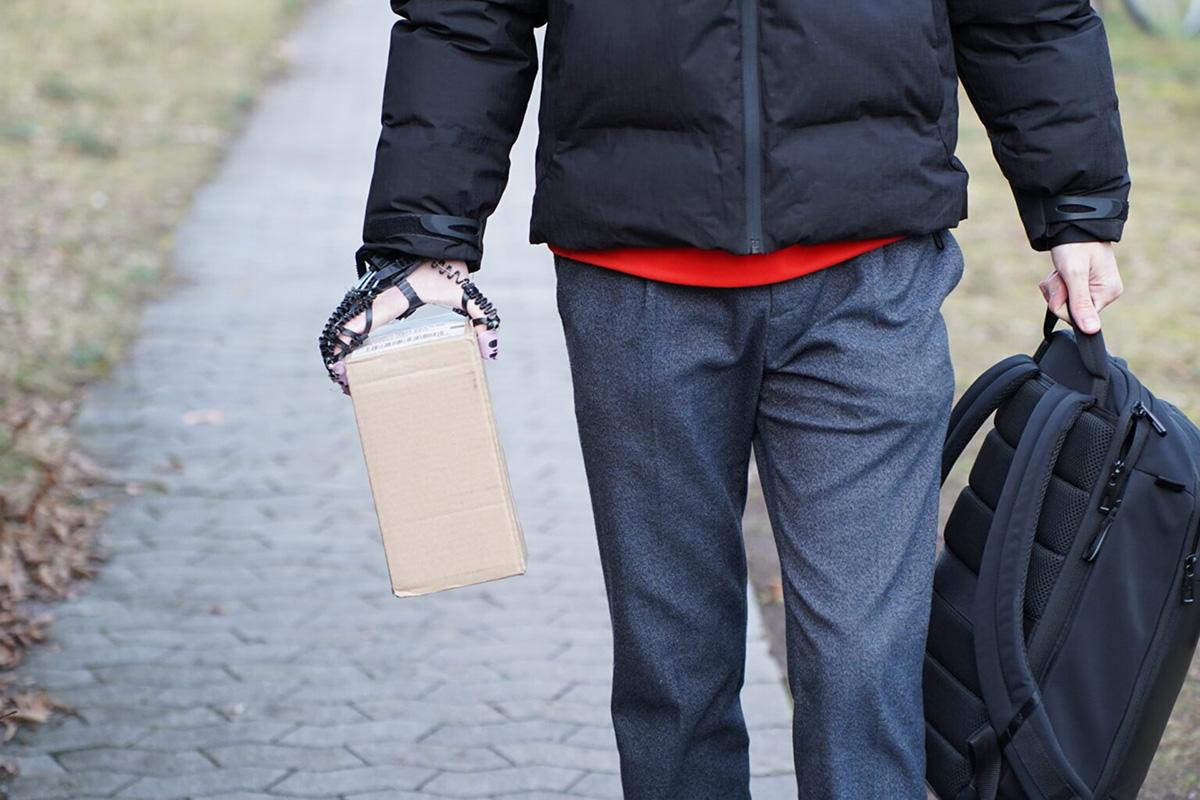 One person is holding a backpack in one hand and a small package in the other, with the help of a brace.