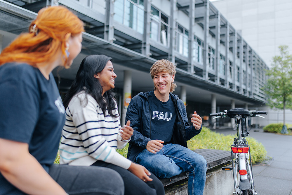Three people are sitting on a bench in front of a building and talking.